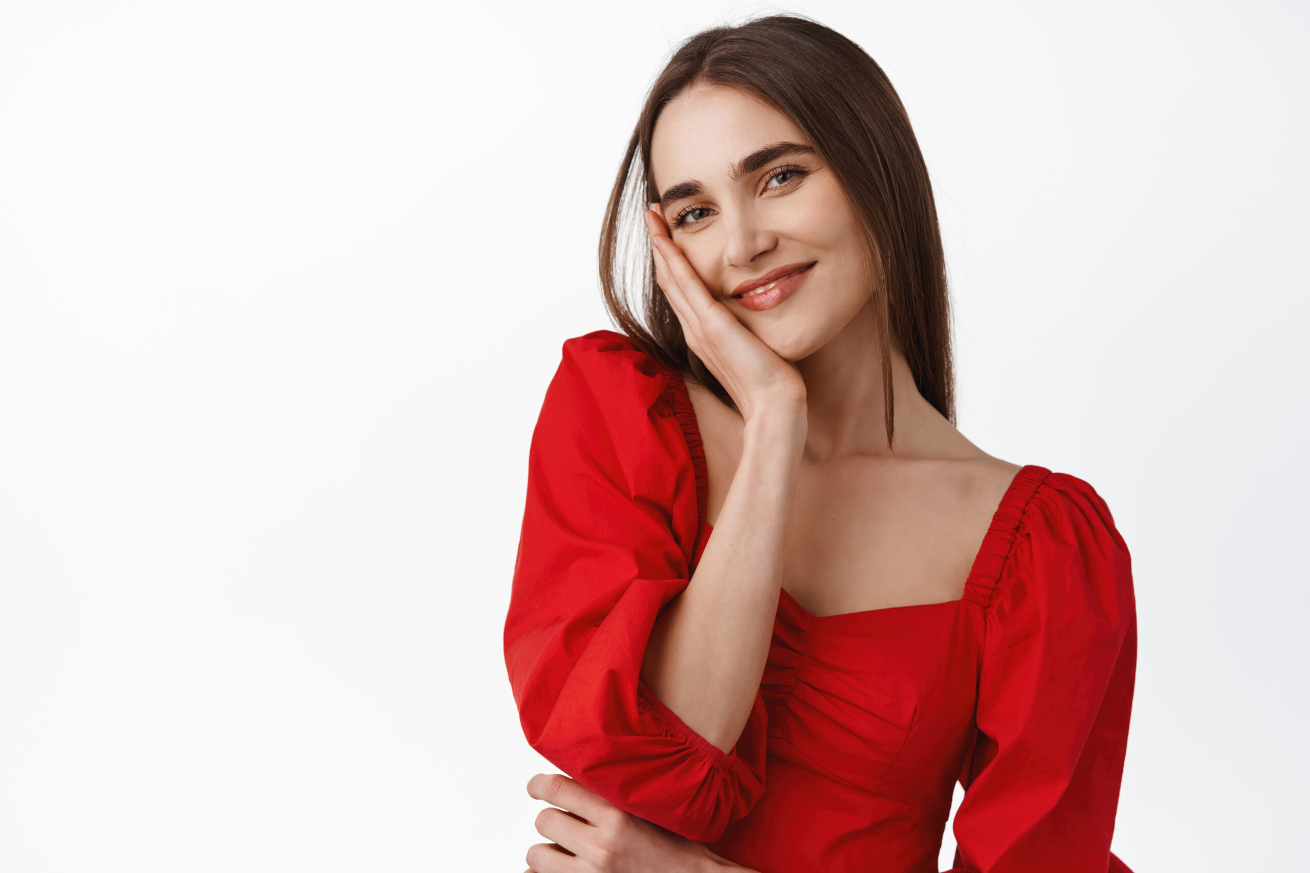 close up of beautiful young woman in stylish red dress, glamour romantic outfit for date or evening party, gazing coquettish and smiling at camera, white background